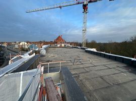 Bautenstand vom 18.03.2026: Die Arbeiten auf der Baustelle entwickeln sich weiterhin sehr positiv. Der Rohbau ist vollständig abgeschlossen, sodass das Gebäude mit eingebauten Fenstern und Haustüren bereits seine endgültige Form erkennen lässt. Damit ist ein wesentlicher Meilenstein in der Projektentwicklung erreicht. Auch im Bereich der Dacharbeiten wurden entscheidende Fortschritte erzielt: Sämtliche vorbereitenden Maßnahmen sind abgeschlossen, aktuell erfolgt die Abdichtung des Hauptdachs. Parallel dazu schreiten die technischen Ausbaugewerke zügig voran. Die Elektroinstallation sowie die Arbeiten in den Bereichen Heizung, Sanitär und Lüftung sind bereits weit fortgeschritten und werden planmäßig in den oberen Geschossen fortgeführt. Im Innenausbau zeigt sich ebenfalls ein hoher Fertigstellungsgrad. Die Trockenbauarbeiten sind größtenteils umgesetzt, erste Bereiche bereits geschlossen. Die Dämmarbeiten im Keller stehen kurz vor dem Abschluss, und die Stahlzargen für die Innentüren wurden erfolgreich eingebaut. Darüber hinaus sind die Estricharbeiten im Kellergeschoss abgeschlossen und werden derzeit im Erdgeschoss fortgeführt. Zeitgleich haben die Fassadenarbeiten begonnen, wodurch das Gebäude auch äußerlich zunehmend Gestalt annimmt. Insgesamt verläuft die Umsetzung des Projekts planmäßig und entspricht unseren hohen Qualitätsansprüchen.